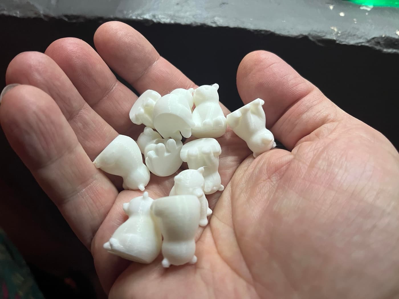 A hand holds several small, white, bear-shaped objects, resembling toys or charms, laid out in the palm.