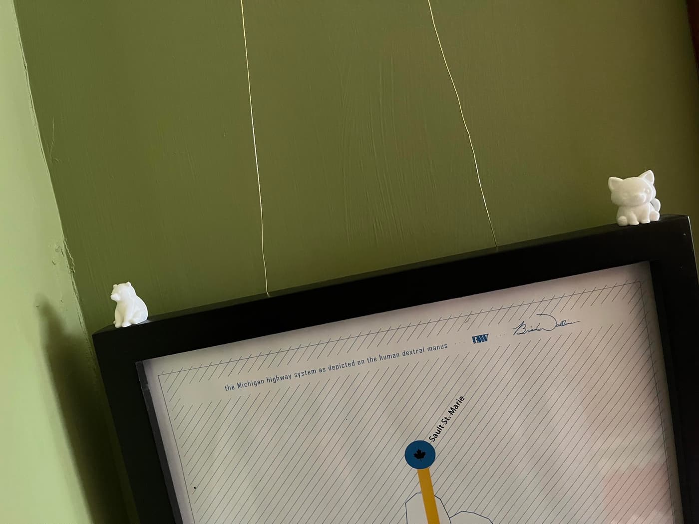 The image features a map displayed on a wall-mounted frame, with a green background. Two small white figurines, one resembling a bear and the other a cat, are positioned on top of the frame.