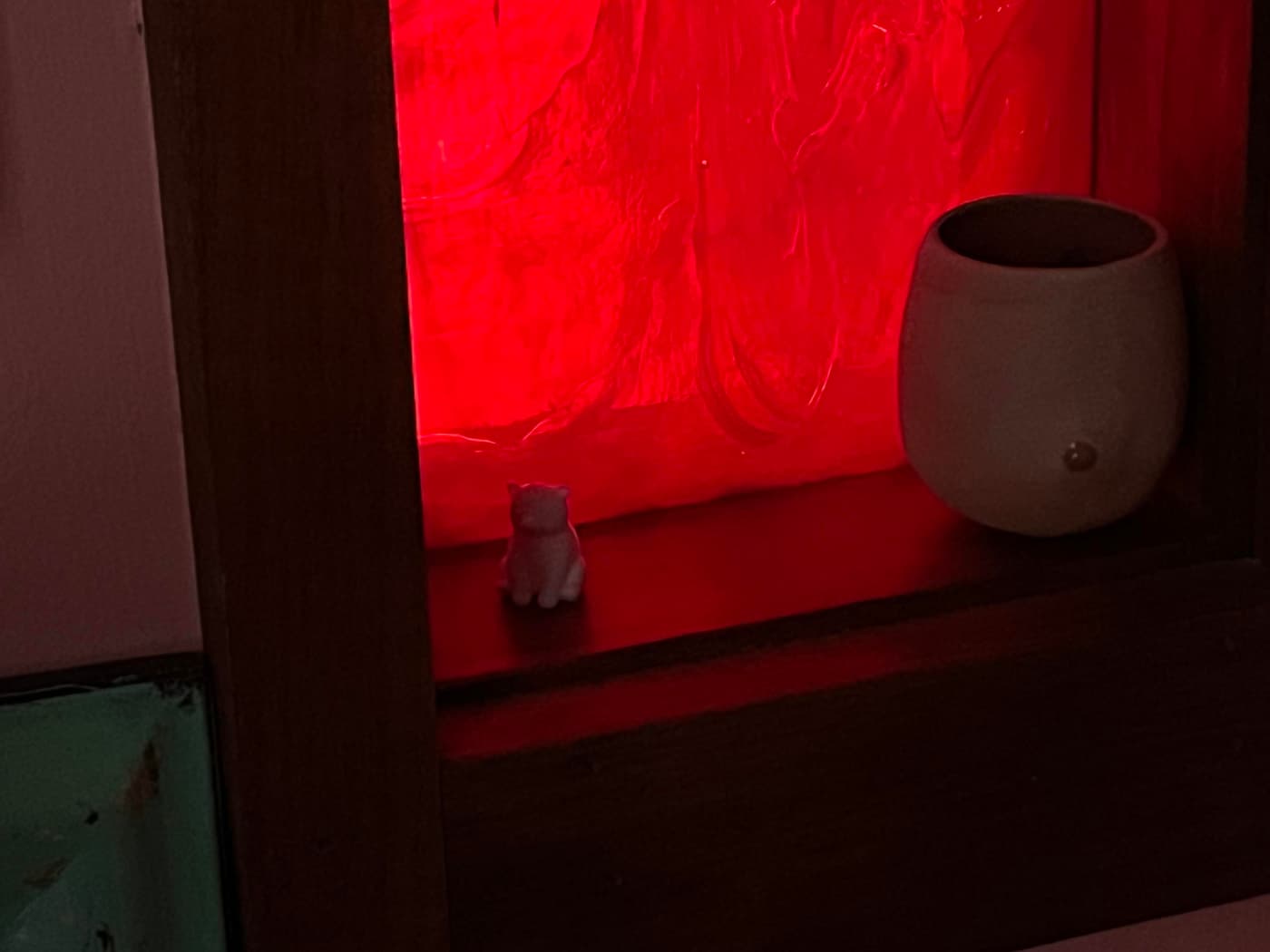 A small white cat figurine sits on a shelf next to a round, beige pottery vase. The background is illuminated with a red glow, enhancing the warm ambiance