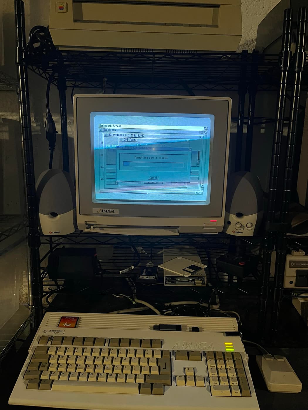 An Amiga computer setup featuring a monitor displaying a Workbench screen with a formatting process