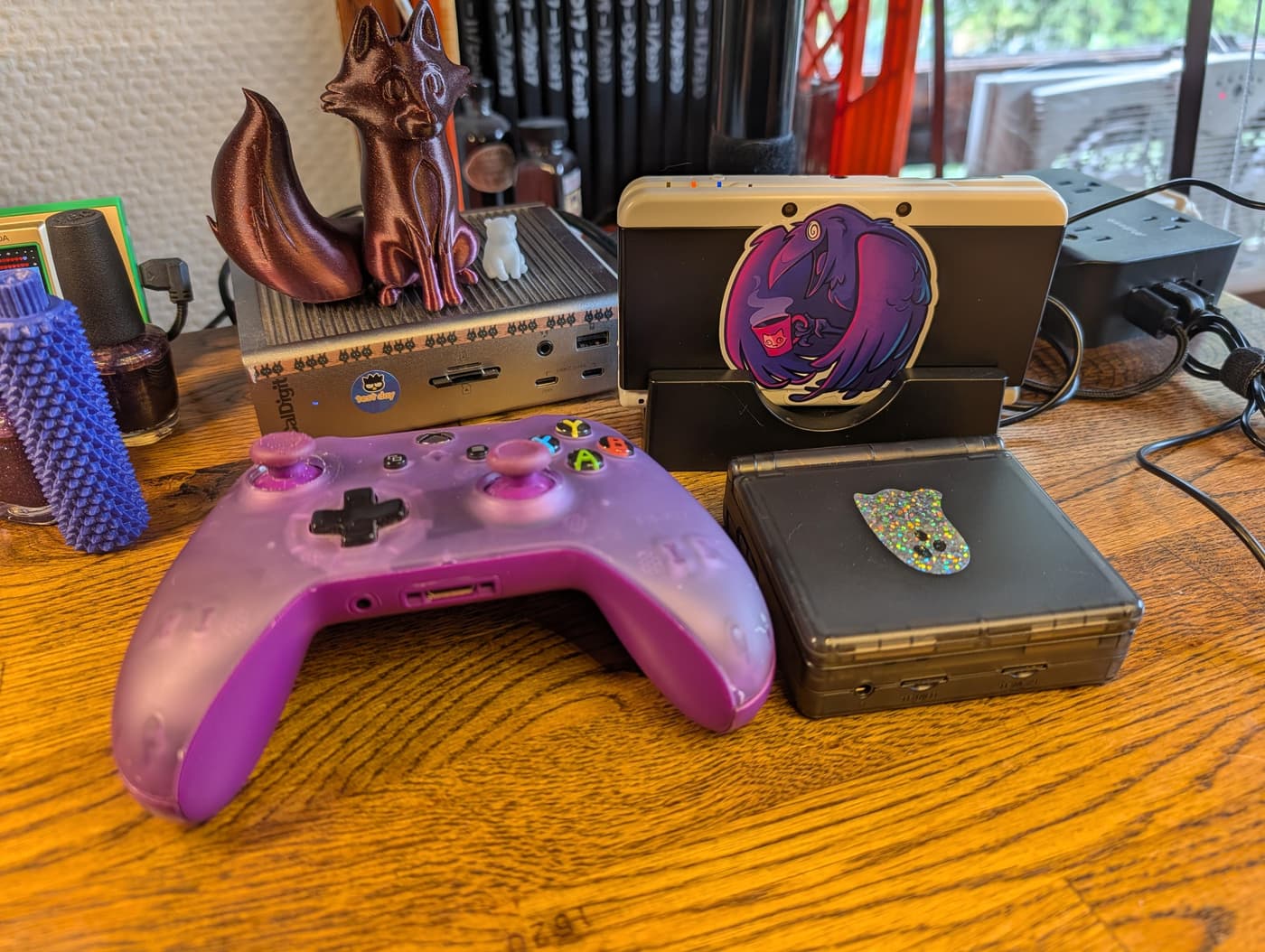 A purple Xbox controller, handheld game consoles, and 3D-printed figurines on a wooden desk