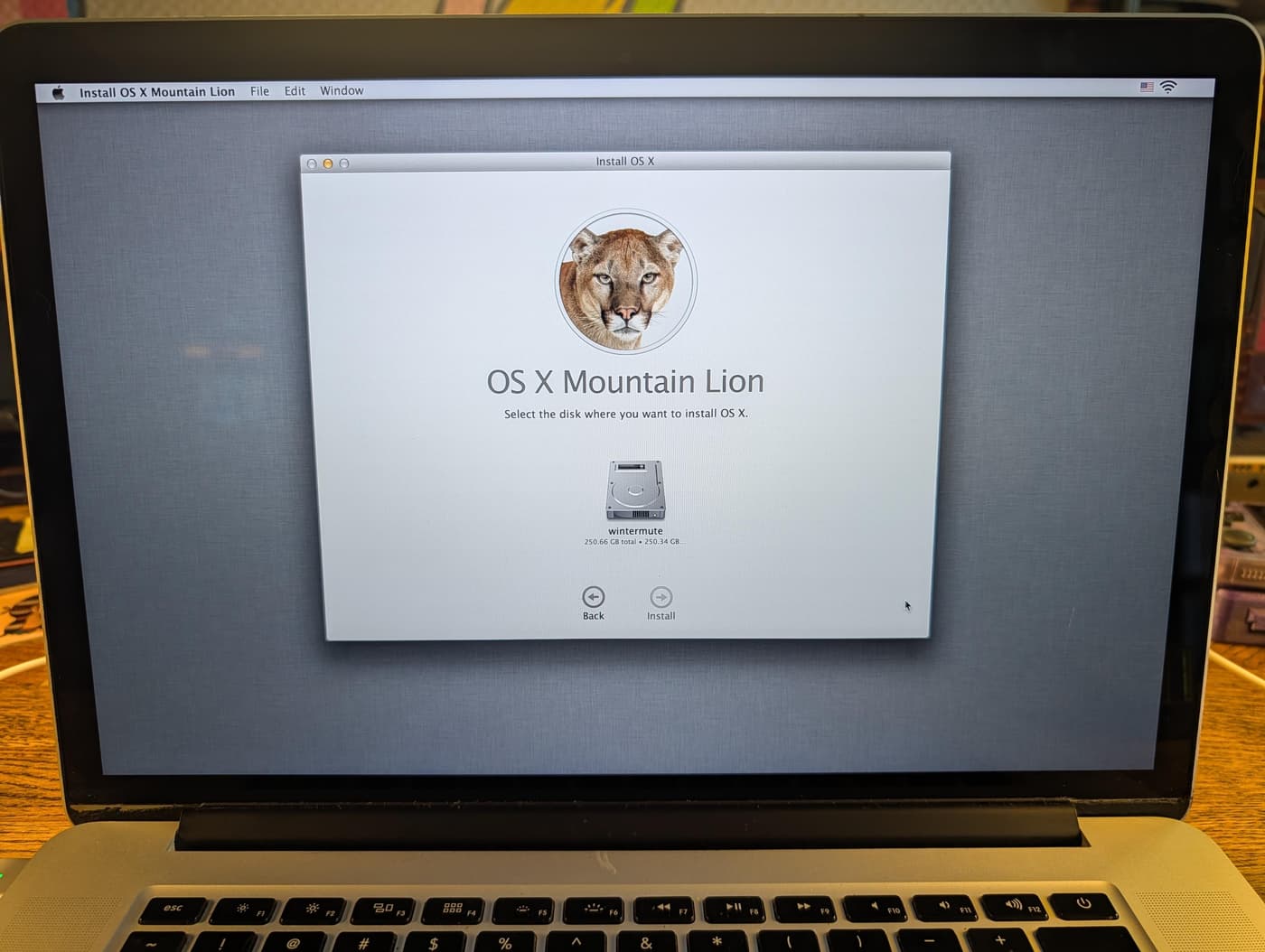 A laptop screen showing the OS X Mountain Lion installer, prompting the user to select an installation disk
